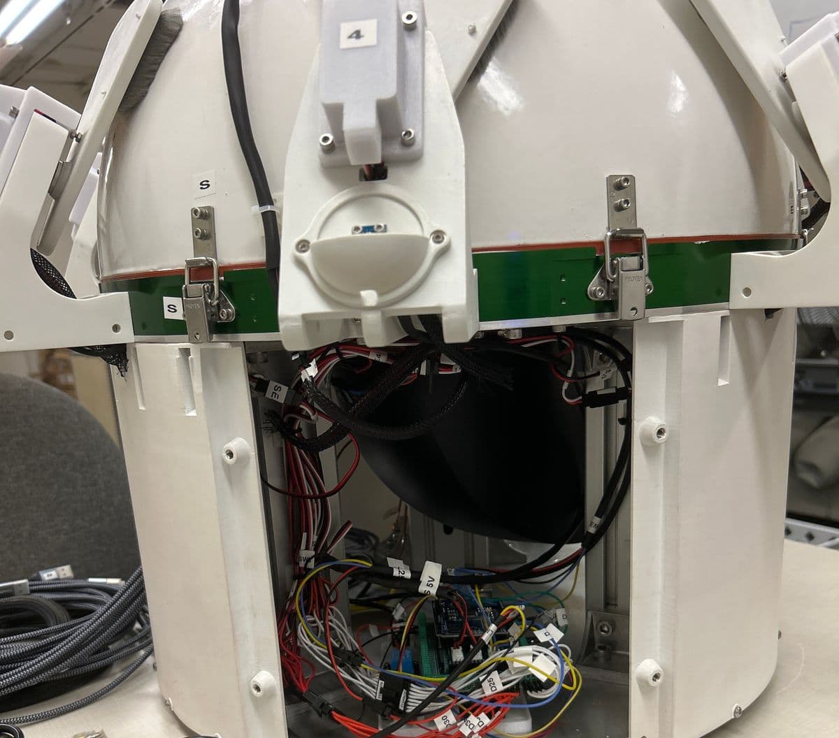 A larger camera enclosure on a bench with a side panel removed, showing a dense harness of labeled wires running to an Arduino with a screw-terminal shield, a relay, and a large fan duct. A shade housing numbered 4 sits above a small half-dome sensor window.
